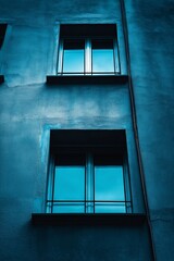 Obraz premium A blue-toned wall features windows, capturing urban life’s reflective and architectural beauty.