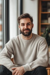 A confident young man with a beard and casual attire enjoys a cozy indoor environment.