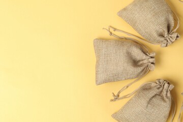 Natural burlap bags on yellow background, flat lay. Space for text