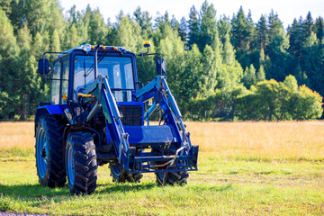 Blue tractor mowing grass in field on summer sunny day