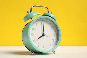 One turquoise alarm clock on white wooden table against yellow background