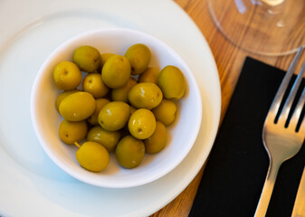 Bowl filled with pickled green olives with bones, popular healthy snack