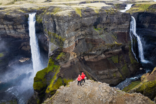 Majestic aerial drone view standing two people in red jackets over Haifoss and Granni waterfalls in Iceland cascading in rugged canyon setting