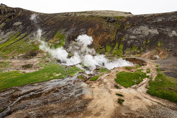 Aerial view of steaming geothermal area amid verdant slopes in a volcanic landscape near Reykjadalur Hot Spring Thermal River in Iceland