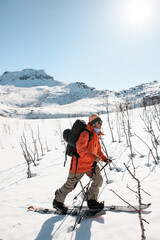 Side view of male skier in orange jacket skiing up snowy slope