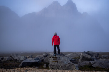 Solitary hiker in red jacket standing amid foggy Vestrahorn mountainous landscape breathtaking...