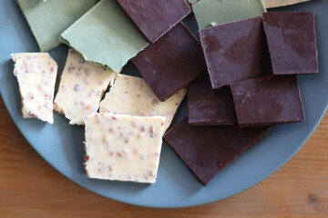 Plate with dark, white and matcha chocolate pieces. Top view, wooden background.
