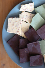 Plate with dark, white and matcha chocolate pieces. Top view, wooden background.
