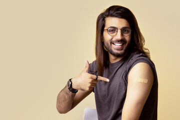 Handsome millennial long-haired indian man got vaccinated against COVID-19, pointing at shoulder...