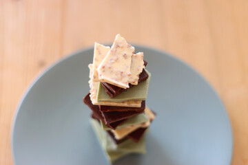 Pile of various chocolate pieces on a plate. Dark, white and matcha chocolate. Selective focus.