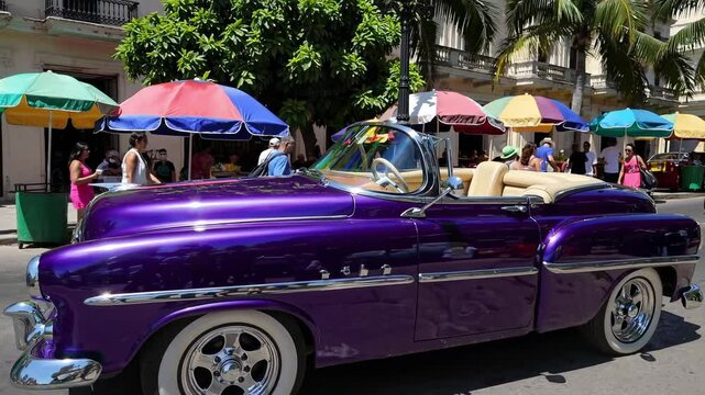 Shiny purple vintage convertible slowly drives through Havana's colorful street market, showcasing classic charm amidst bustling vendors and locals