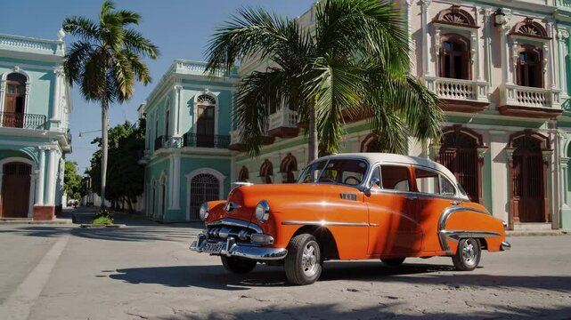 Vintage orange classic car parked alongside colorful colonial architecture and swaying palm trees, capturing nostalgic Cuban urban landscape with vibrant street scene in Havana