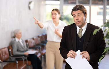 ..Upset adult man in business suit with documents in his hands being criticized in office