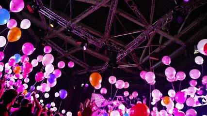 Colorful balloons rising, illuminating excited concertgoers' faces while creating vibrant, electrifying atmosphere during live music performance