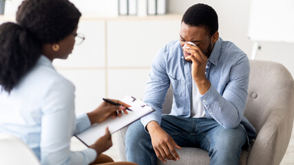 Depressed black guy crying at psychotherapist's office, seeking professional help at clinic....