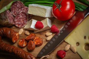 Bright sliced sausages and cheeses with vegetables and herbs lie on a board