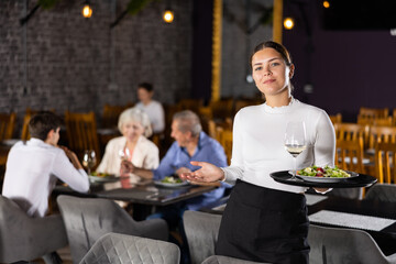 Young female waitress in uniform posing with tray in her hands in restaurant