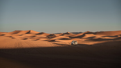 White off road vehicle navigating the mesmerizing erg chebbi dunes in merzouga desert, morocco, under the vast expanse of the late afternoon sky