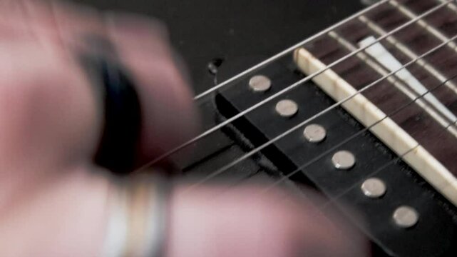 Mano derecha de guitarrista, tocando las cuerdas con una plumilla.