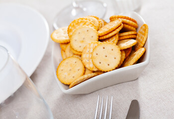 Bowl with tasty thin round salted crackers on table