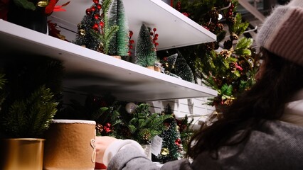 The woman selects Christmas home decor from artificial pine tree branches in pots, creating a festive and cozy holiday atmosphere.