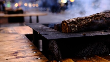 A glowing log burns gently in a stylish fire pit, creating a warm and festive atmosphere at a Christmas market while providing cozy heat for visitors on a chilly winter evening.