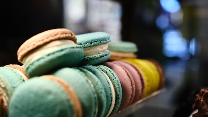 Close-up colorful macarons with white cream filling displayed under soft lighting on a countertop with a blurred background and selective focus highlighting their delicate texture and vibrant hues