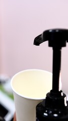 Barista adds red cherry syrup to a white paper coffee cup using a dispenser at coffee shop creating delicious flavored drink with vibrant color perfect for coffee lovers seeking refreshing beverages