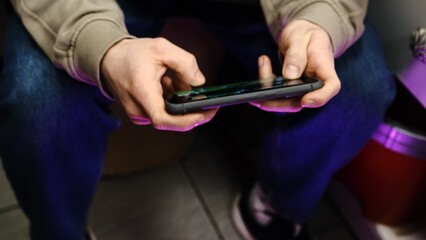 Young man playing mobile game with fast finger movements and colorful pulsating hand lights, dynamic gameplay, close up phone screen, digital entertainment, gaming action, energetic gaming session.