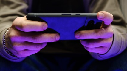 Young man playing mobile game with fast finger movements and colorful pulsating hand lights, dynamic gameplay, close up phone screen, digital entertainment, gaming action, energetic gaming session.