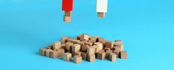 Magnet attracting wooden cubes on light blue background, closeup