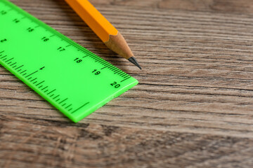 Green ruler and pencil on wooden table, closeup. Space for text