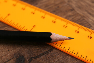 Orange ruler and pencil on wooden table, closeup
