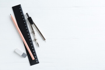 Ruler, pencil, eraser and compass on white wooden table, flat lay. Space for text