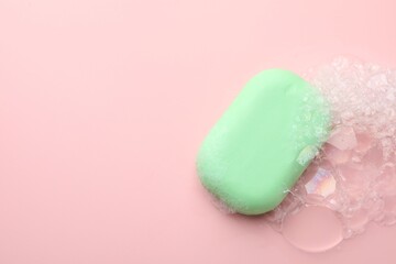 Soap bar with foam on light pink background, top view. Space for text