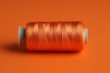Spool of sewing thread on orange background, closeup