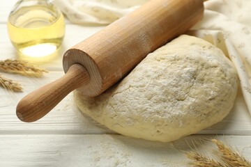 Fresh dough, rolling pin, oil and spikes on white wooden table, closeup