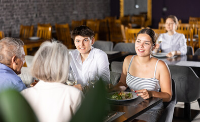 Young family and elderly couple of spouses eating in restaurant celebrating important event and communicating. Cozy sparsely populated restaurant, festive lunch, wine tasting