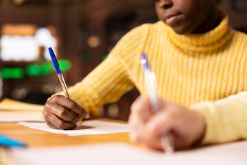 Diverse preteens writing class notes in their notebooks at a library desk, preparing for an academic assessment after classes. Literary ideas on paper, emphasizing child development. Close up.