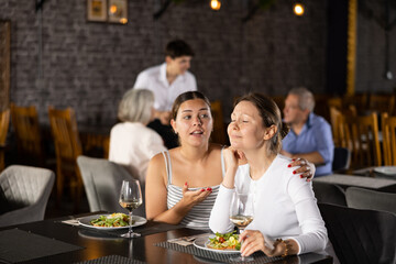 Young woman comforting upset female friend during friendly meeting over dinner in restaurant