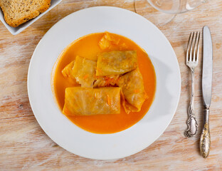 Homemade cabbage rolls in leaves of cabbage at plate with sour cream and greens