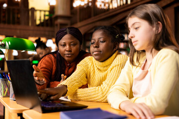 African american professor helping elementary students to practice writing essays and completing homework in a library filled with learning resources. Tutoring session for academic success.