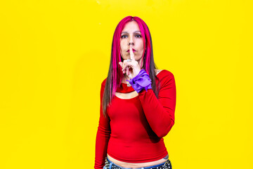 Woman with pink hair making silence gesture on yellow background