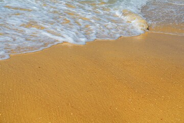 The image displays gentle waves rolling onto a sandy beach. The vibrant blue water meets warm golden sand, creating a peaceful coastal scene that invites relaxation and tranquility.