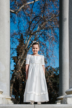 Girl in first communion dress standing among columns