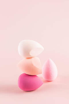 Balanced stack of colorful makeup sponges on pink background