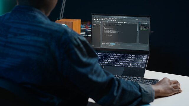 Software developer writes code on laptop screen while in apartment office using Java programming languages. Programmer remotely working on fixing database errors while working from home, camera A