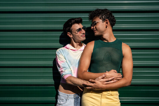 Affectionate gay couple embracing against green wall on a sunny day
