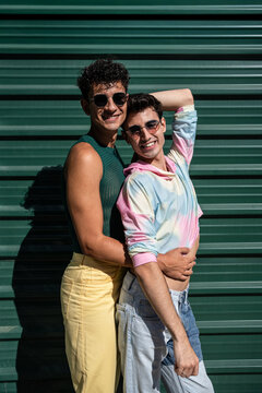 Affectionate gay couple embracing against green wall on a sunny day