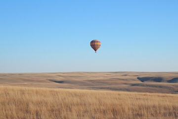 Obraz premium Colorful hot air balloon soaring above golden grasslands under a clear blue sky at sunset